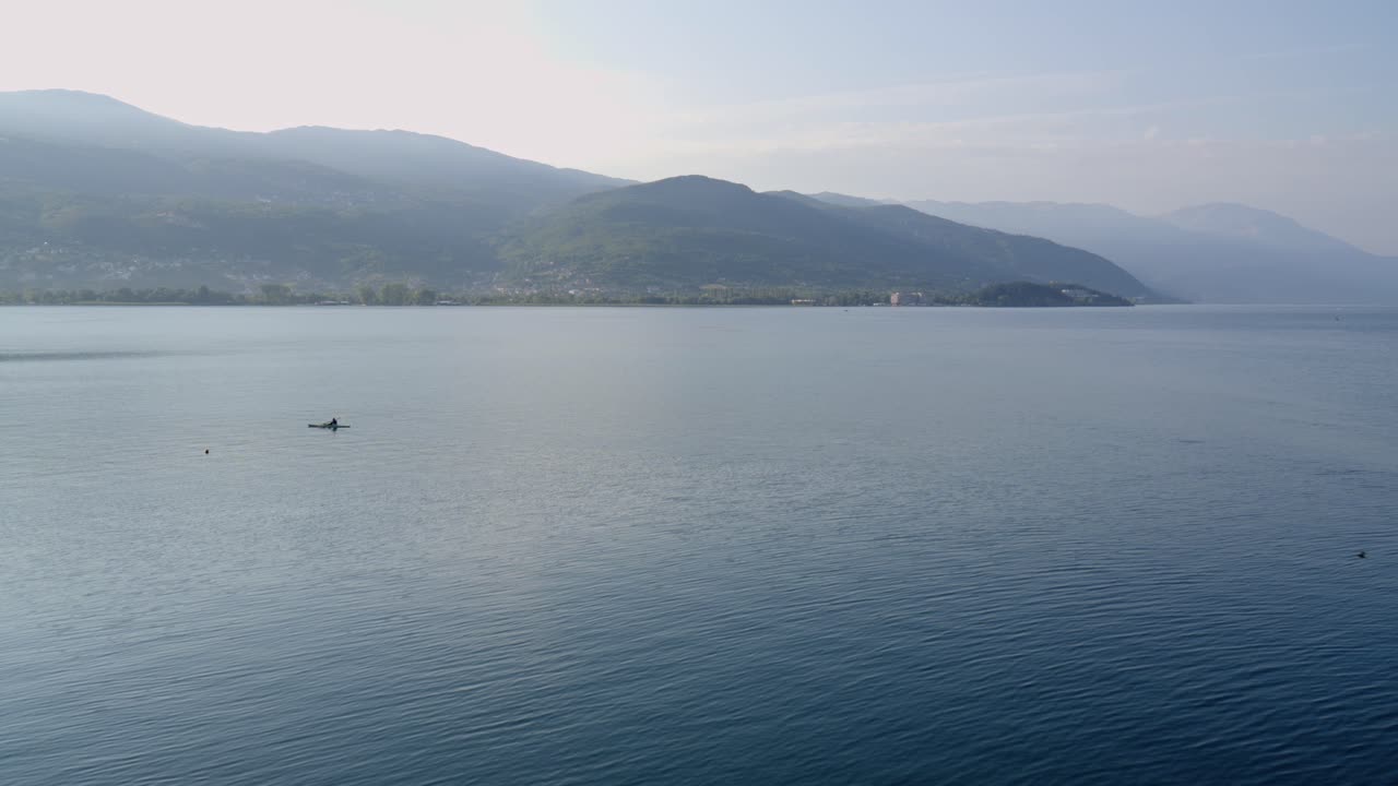 A lone paddler kayaks across lake Ohrid, tranquil morning, wide shot