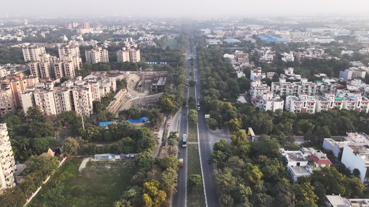 Vista aerea dall'alto della rete stradale di Greater Noida, dove auto e autobus attraversano una lussureggiante vegetazione, che riflette un paesaggio urbano calmo ma attivo
