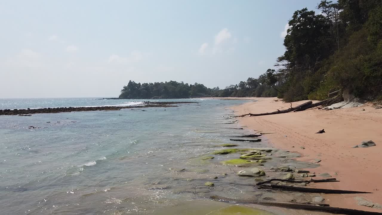 Un'ampia veduta di una spiaggia remota ai tropici mentre la marea si ritira rivelando coralli, scogliere e antiche formazioni rocciose vulcaniche
