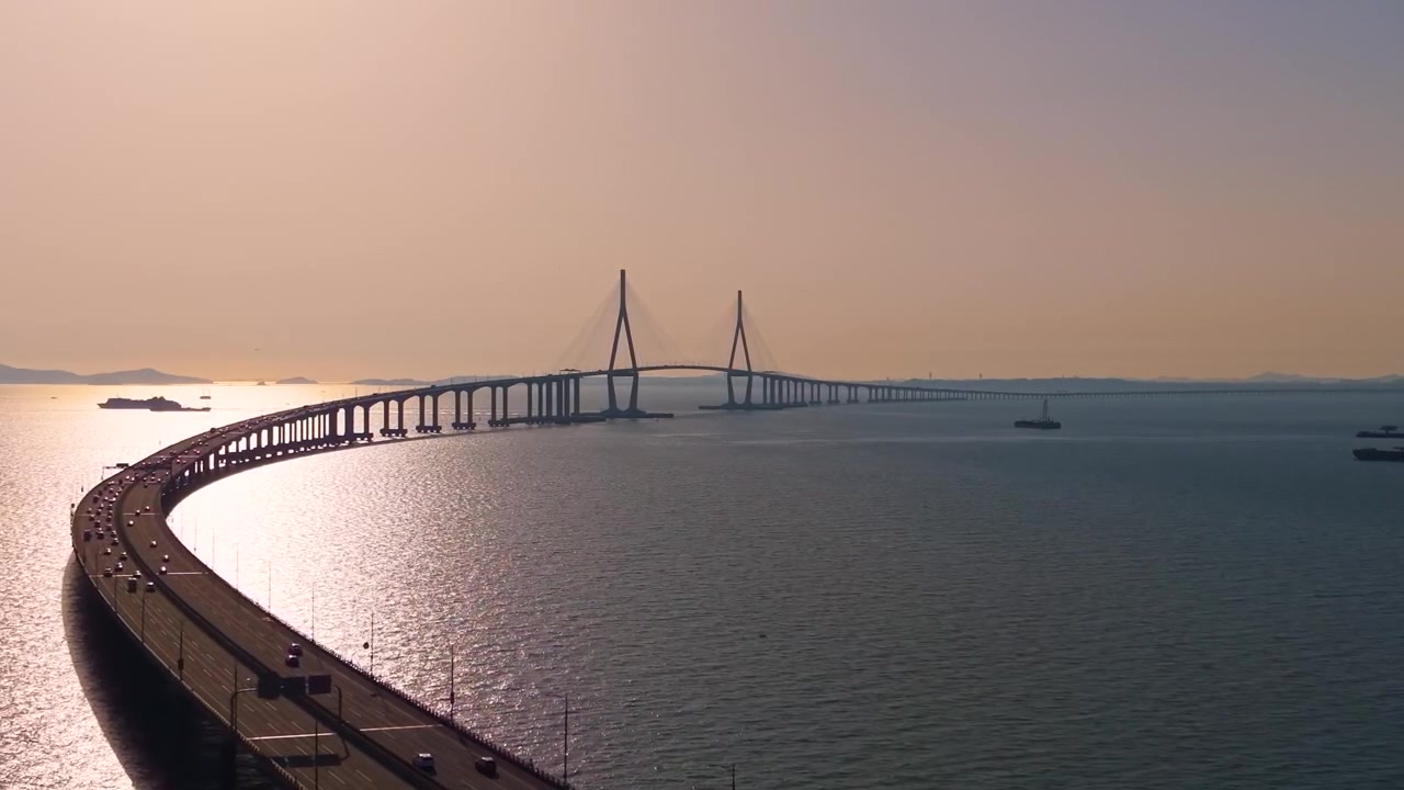 Il Ponte di Incheon si curva elegantemente sul mare, stagliandosi contro il cielo dorato del tramonto, con i fari del traffico che scorre sotto.