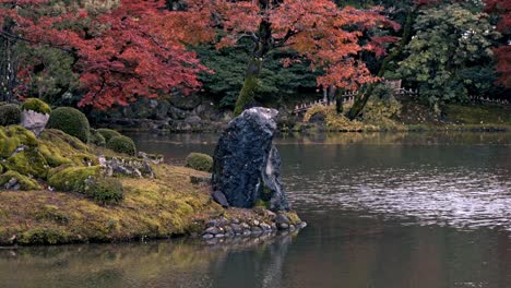 kanazawa's kenroku-en gardens lake at sunset with red foliage in autumn, japan