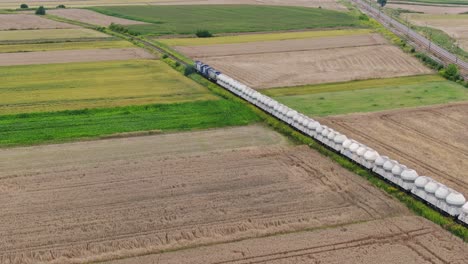tren de carga con vagones de silo se mueve a través de campos en la zona rural de polonia europa, aéreo