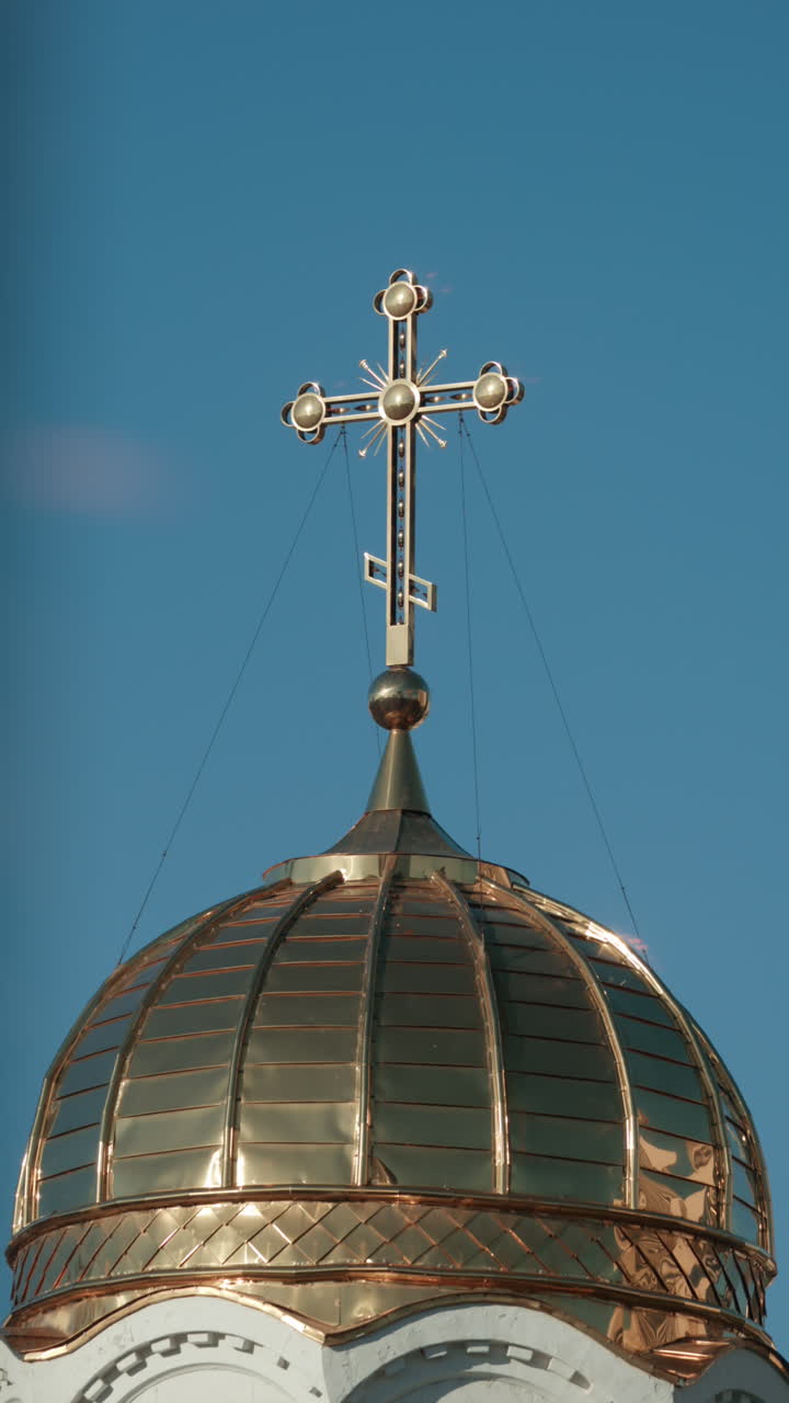 Elegant metallic church cross glowing under clear blue sky. Vertical