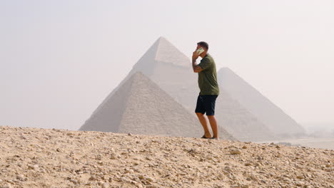 un hombre hablando por teléfono mientras está en la meseta de giza, con vistas a las pirámides en el cairo, egipto - foto de mano