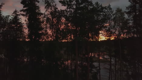 wide angle aerial shot flying over trees at cabin with beautiful calm lake during sunset