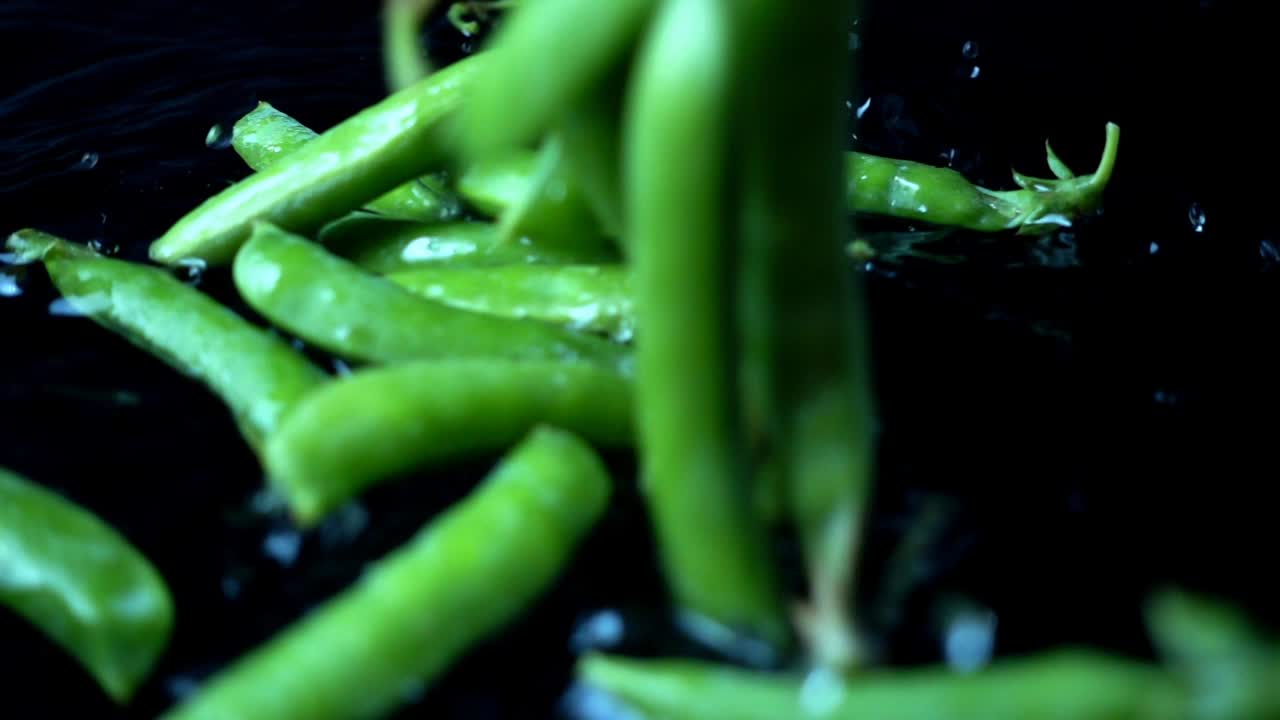 Falling of green peas in water on a black background. Slow motion