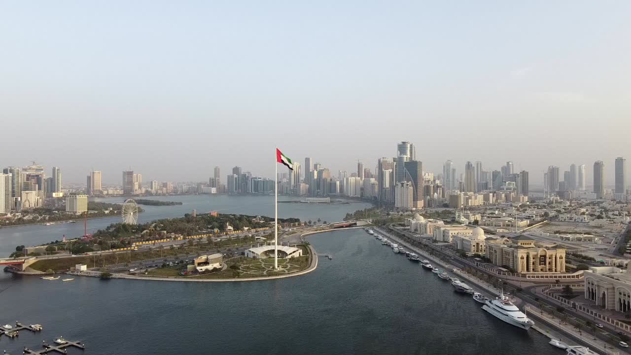 Vista aerea della bandiera degli Emirati Arabi Uniti che sventola con sviluppo urbano sullo sfondo, simbolo nazionale degli EAU sull'Isola della Bandiera di Sharjah.