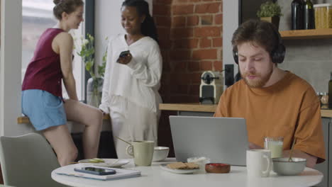 boy with headphones working on laptop computer during breakfast in a shared flat