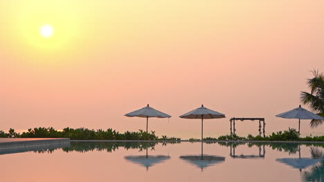 Evening-Sun-Above-Tropical-Beach-and-Luxury-Poolside-With-Parasols-Reflection-on-Pool-Water,-Full-Frame