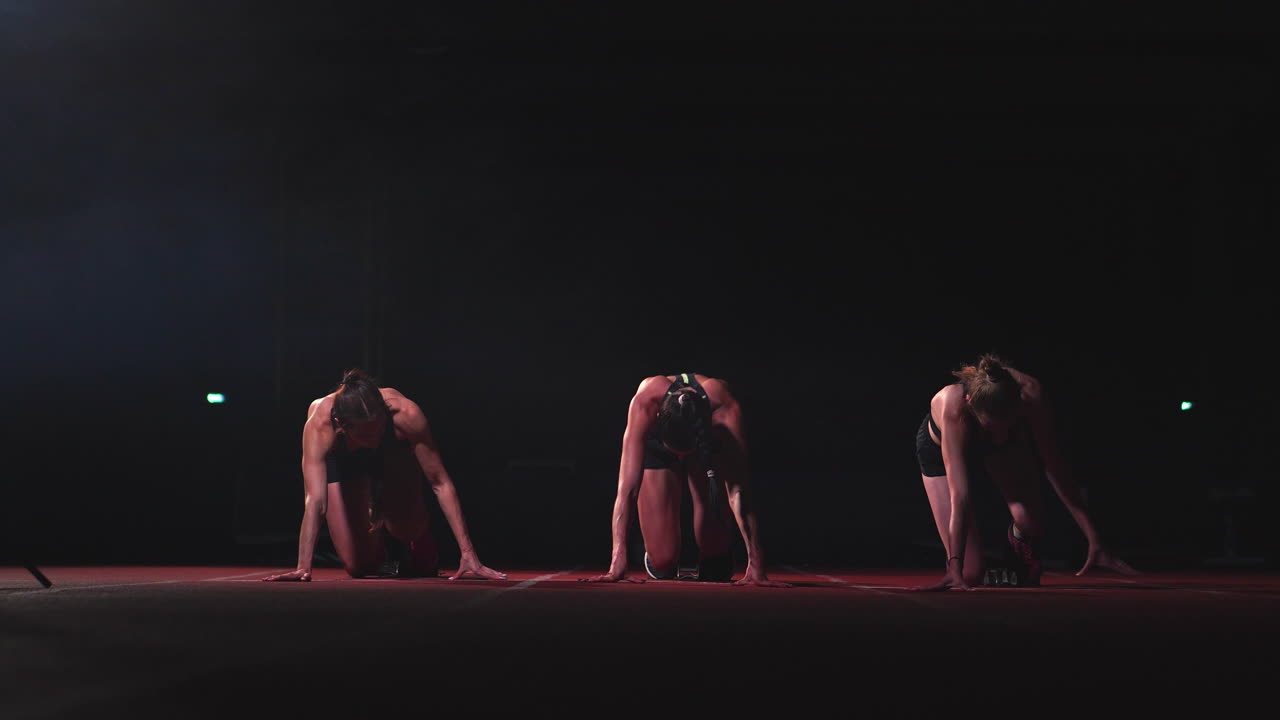 tres chicas vestidas de negro están en las plataformas de salida para comenzar la carrera en la competencia.