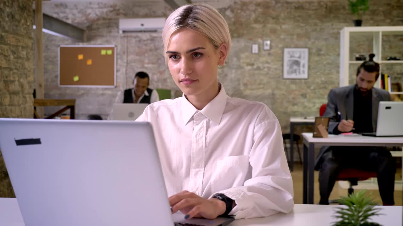 Giovane e felice donna d'affari digita sul laptop in ufficio, i colleghi fanno rete con le tecnologie, concetto di lavoro, concetto di comunicazione