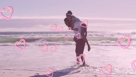 animation of pink hearts over happy african american couple piggybacking on beach