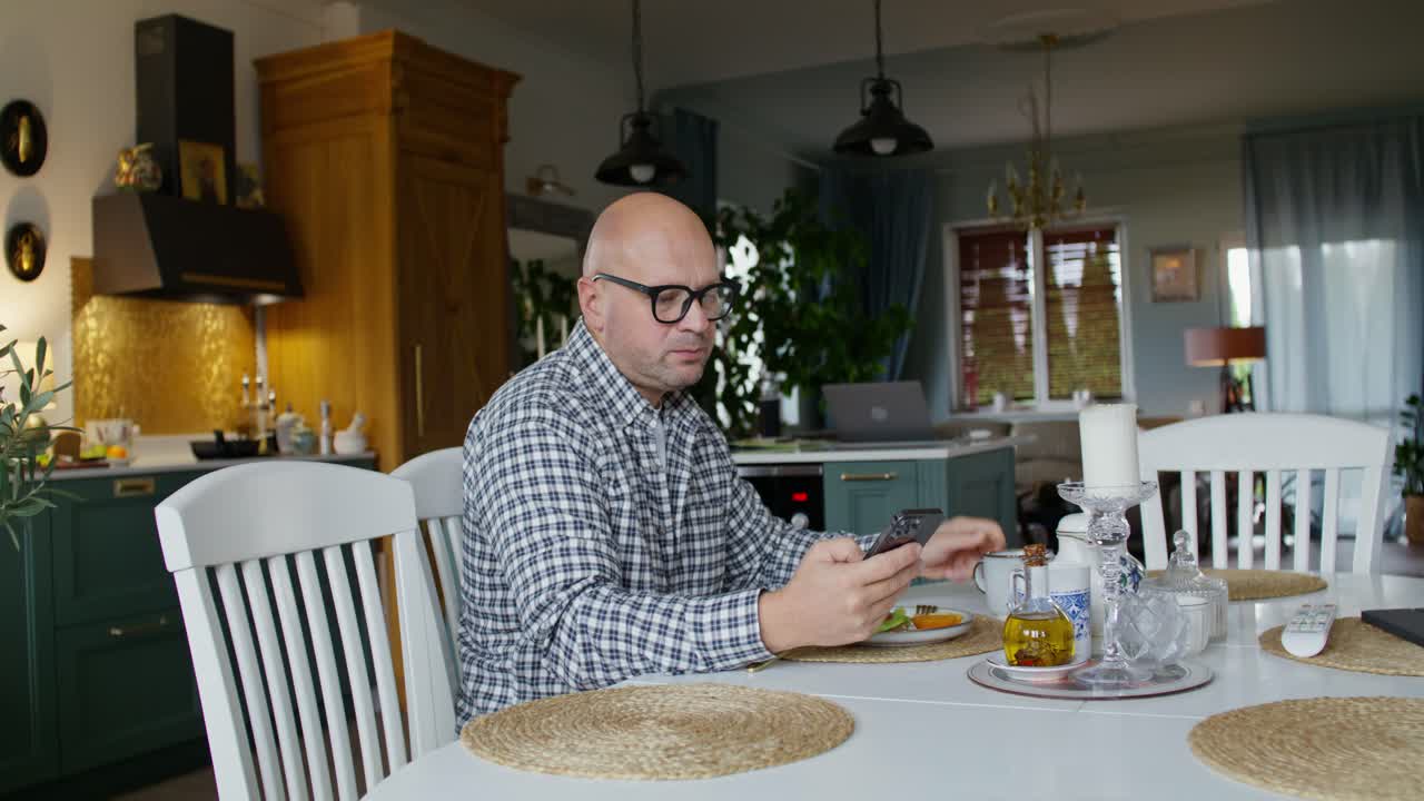 hombre desayunando y usando un teléfono inteligente en una cocina