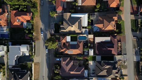 aerial top down shot of driving cars on road in australian residential area during sunset time - establishing drone shot