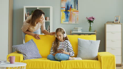 teenage girl with headphones listening to music sitting on yellow sofa while her mother speaks loud to her