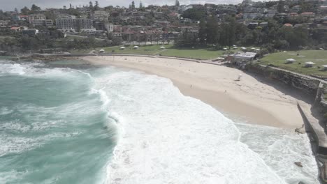 olas oceánicas espumosas que se lavan en tierra - vista panorámica de la playa de bronte en los suburbios del este, sydney, nueva gales del sur, australia - toma aérea de drones