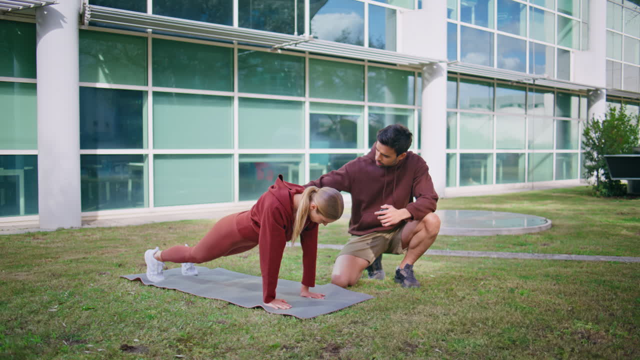 Woman standing plank exercise on fitness mat. Professional coach assisting girl