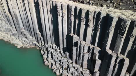 Aerial-drone-forward-moving-shot-over-column-shaped-rocky-pillars-along-icelandic-studlagil-canyon-with-river-flowing-into-basaltic-rock-formation-in-Iceland