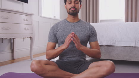 tilting shot of man sitting on yoga mat in bedroom at home stretching and breathing- shot in slow motion