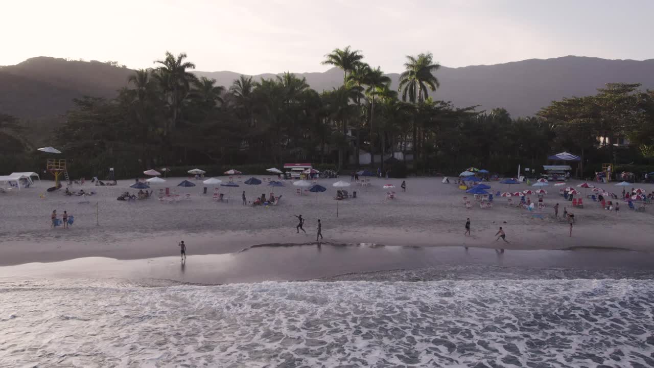 el dron retrocede hacia el océano mostrando la costa, algunas personas y la selva atlántica al fondo