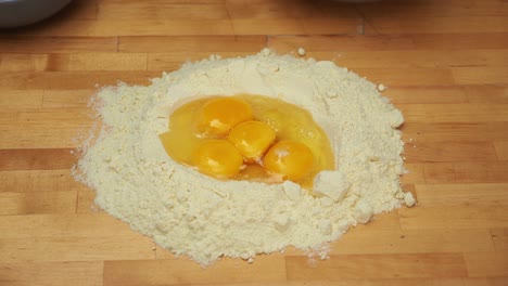 pouring eggs into a mound pile of flour over a wooden surface - high angle medium shot