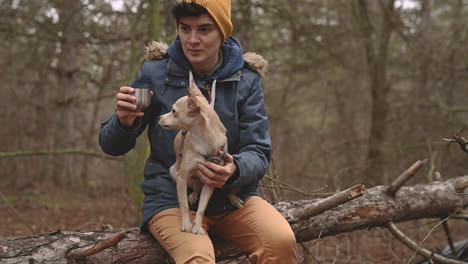 een jonge vrouw met kort haar drinkt een warme drank in het bos