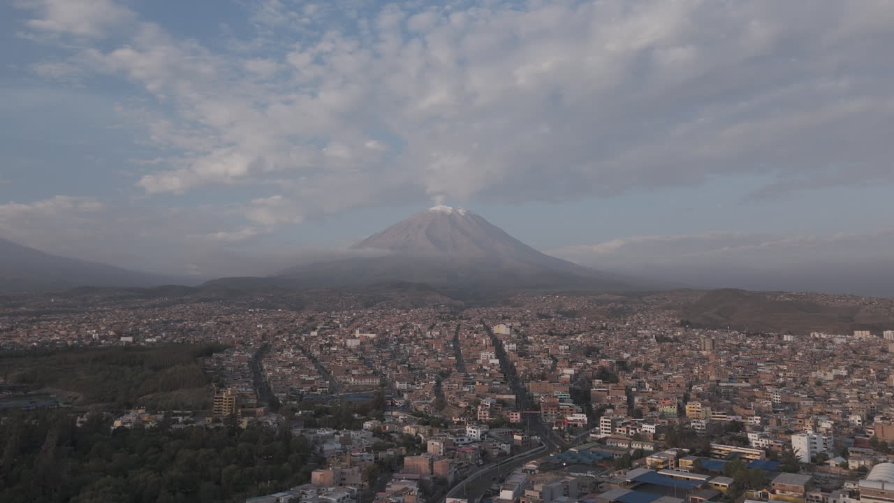 Backwards moving drone shot above Arequipa Peru with view on the mountain near sunset time with clouds in the sky LOG