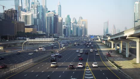 The-active-Dubai's-Sheikh-Zayed-Road-at-dusk,-with-the-metro-passing-beside-the-iconic-skyline-and-bustling-vehicles