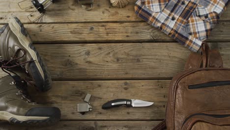 Camping-equipment-with-knife,-lighter,-rucksack,-boots-and-copy-space-on-wooden-background