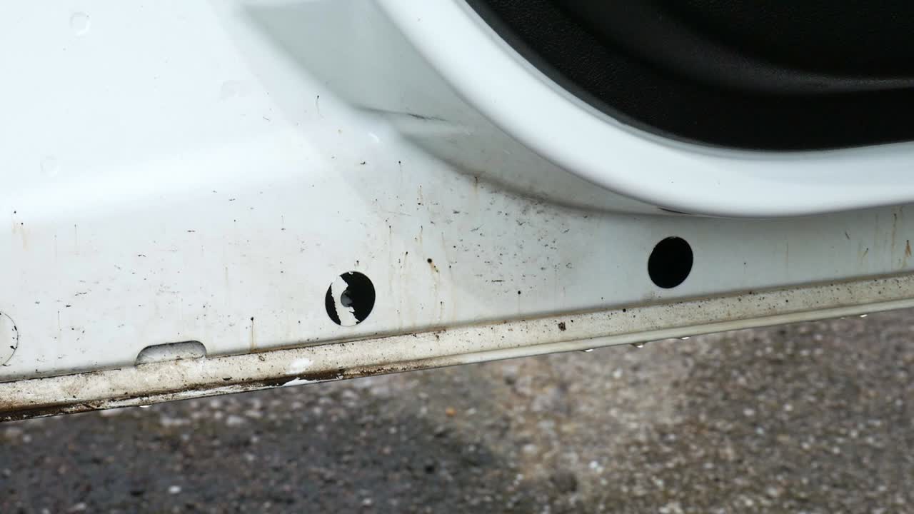 Wiping away tar from the inside of a white van door with a yellow microfiber cloth