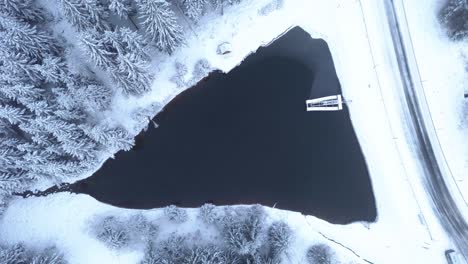Winter-wonderland,-frozen-lake-pull-up-drone-aerial-shot,-a-body-of-water-frozen-in-the-forest