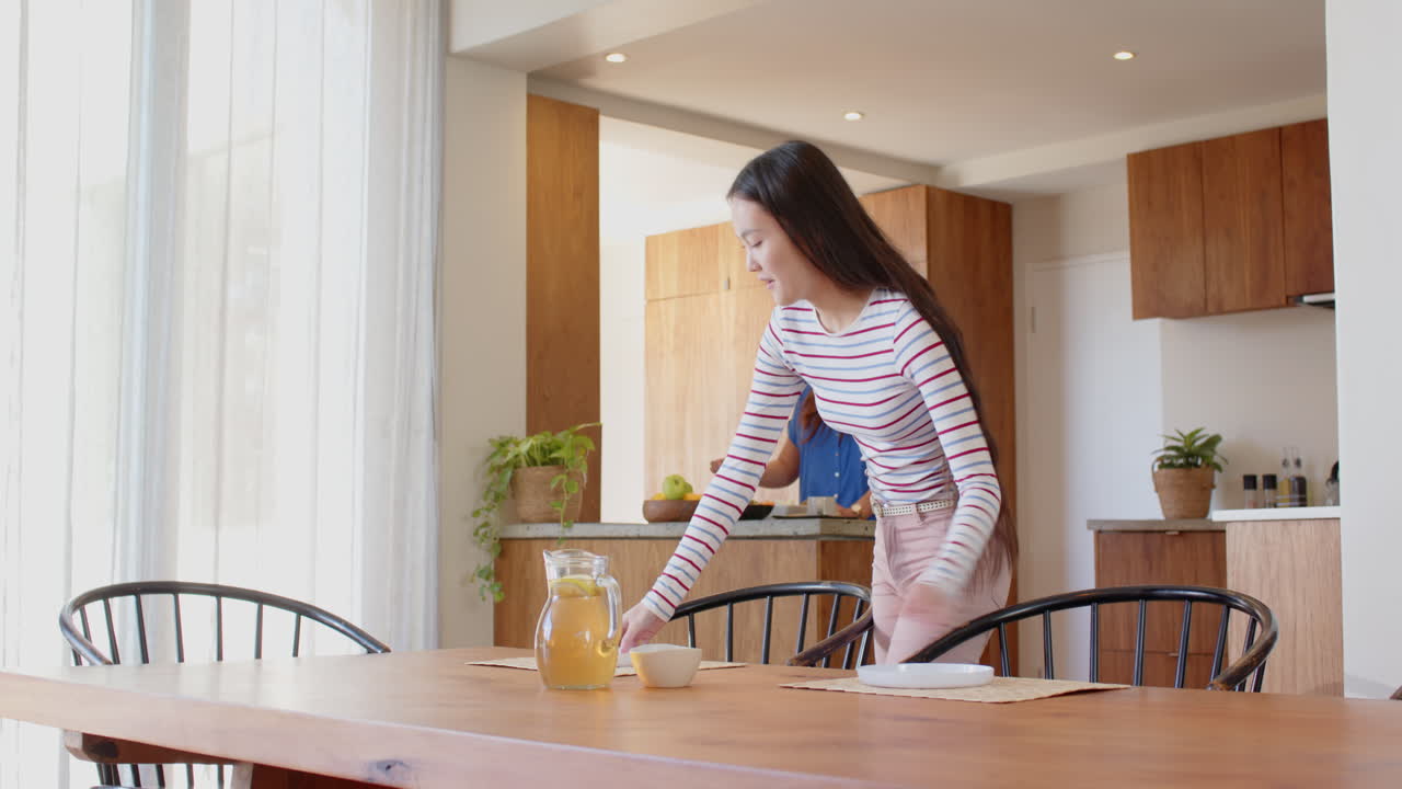 Setting table with tea, young woman preparing meal in modern kitchen