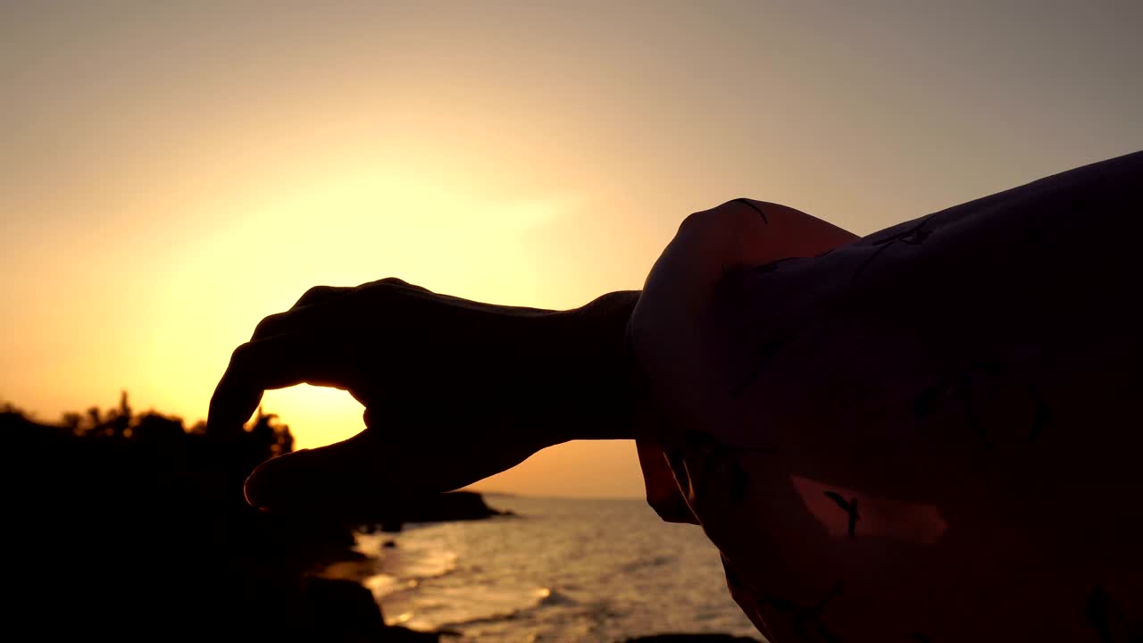 새벽에 해가 뜨는 바다에서 소녀가 놀고 손가락 사이에 빛을 다루고 있습니다.