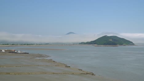 Barcos-De-Pescadores-Atrapados-En-El-Barro-Durante-La-Marea-Baja-En-La-Isla-De-Ganghwado-En-Corea-Del-Sur,-Neblina-Y-Vapor-Sobre-Los-Picos-De-Las-Montañas