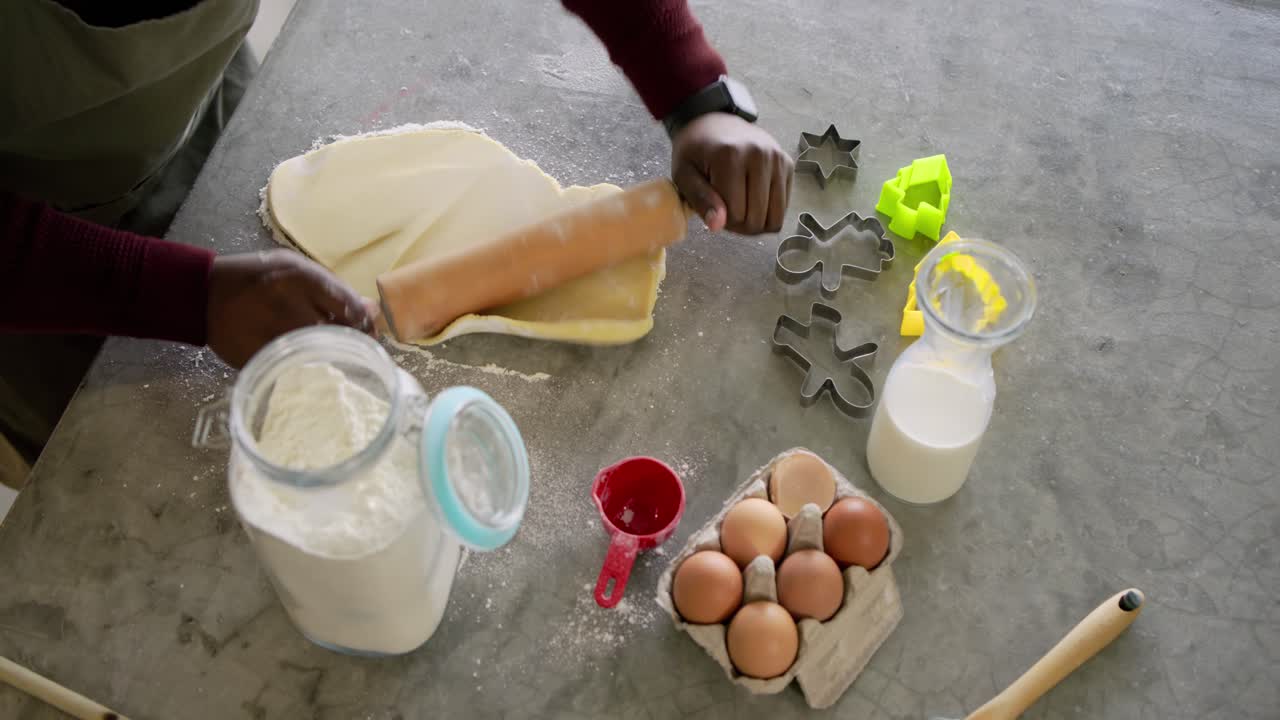 After flattening dough, hands are rolling with pin on counter into thin sheet for cookie cutting