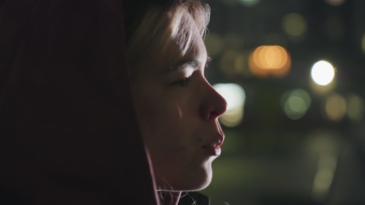 Calm focused woman side view enjoying dinner outdoors at dusk under city lights biting into tossed bread and sipping water after exercise break on bench in urban park at twilight