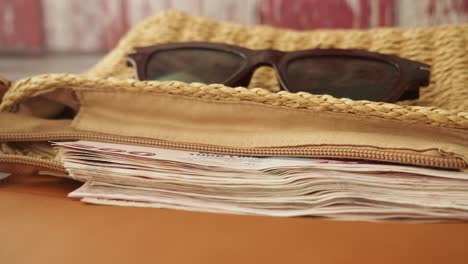 travel funds in a straw bag with sunglasses