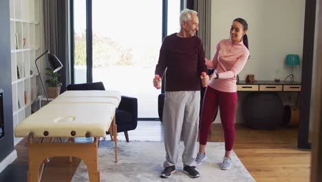 video of happy biracial female physiotherapist exercising with caucasian senior man