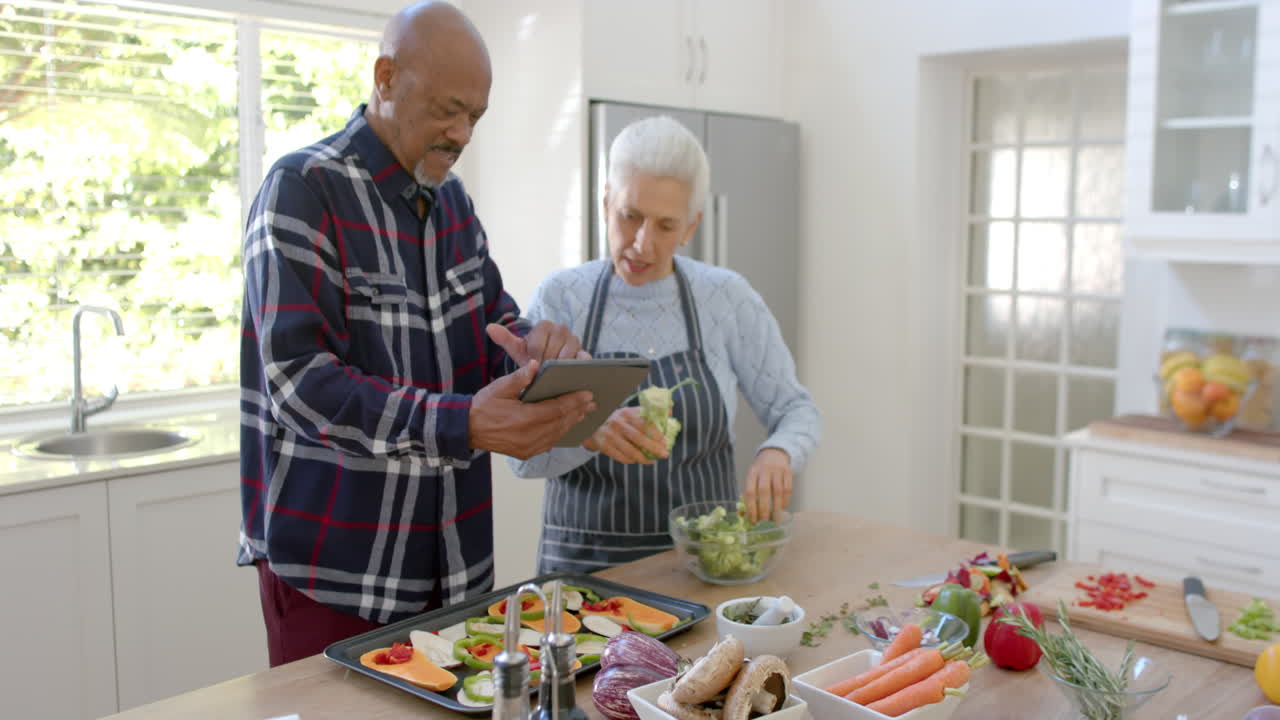 pareja de ancianos feliz preparando verduras, usando tableta en la cocina, espacio de copia, cámara lenta