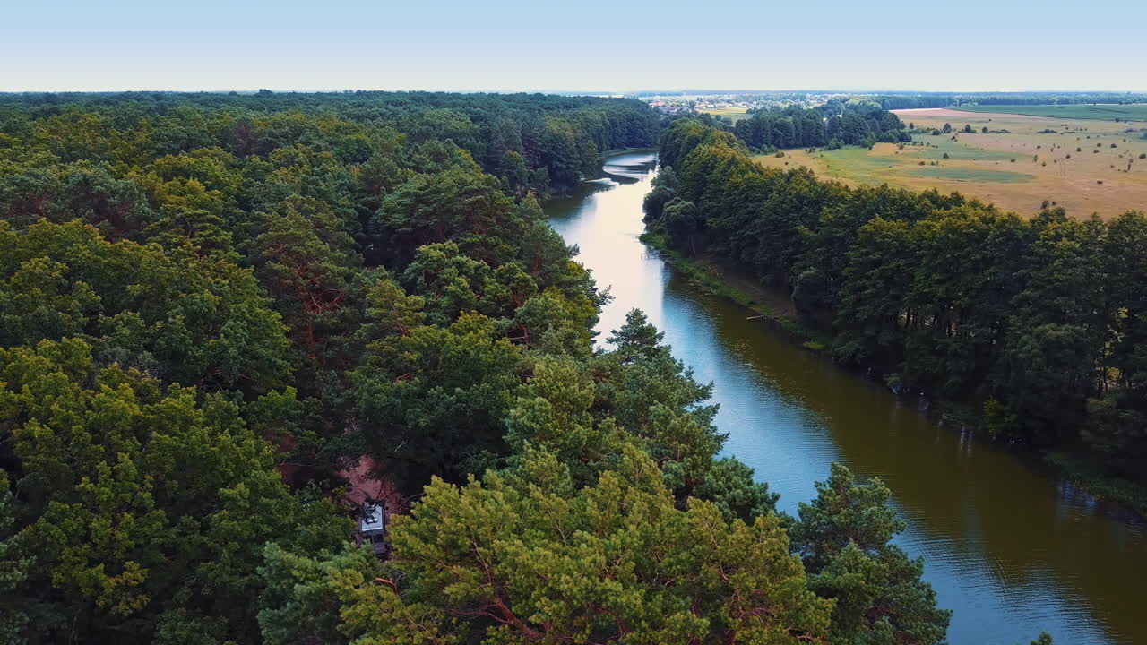 Splendid view of the river flowing in the forest. Narrow river at the farmlands. Car moving by the road in the woods. Top view.
