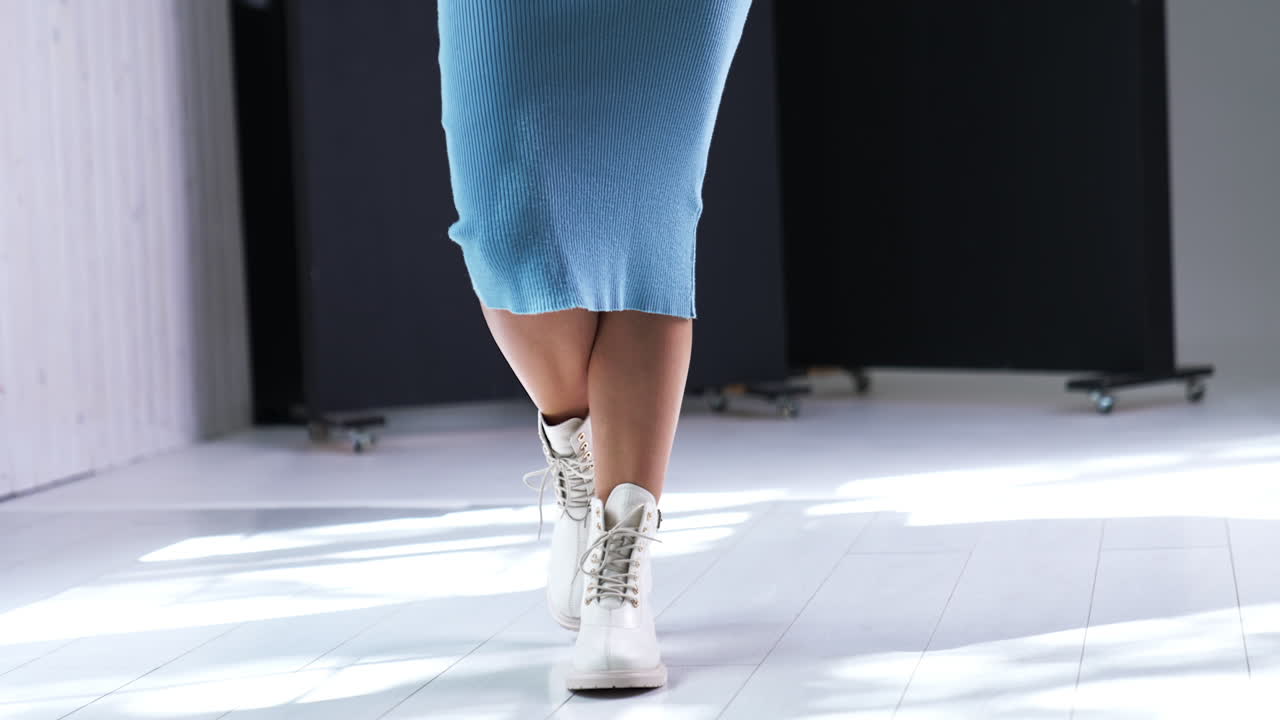 Female in blue midi dress walks by the room. Model demonstrating the boots made of leather, with tractor soles and laces.