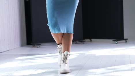female in blue midi dress walks by the room. model demonstrating the boots made of leather, with tractor soles and laces.