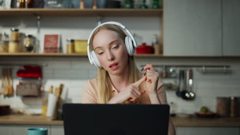 woman teacher lecturing online sitting at kitchen with laptop wearing headphones