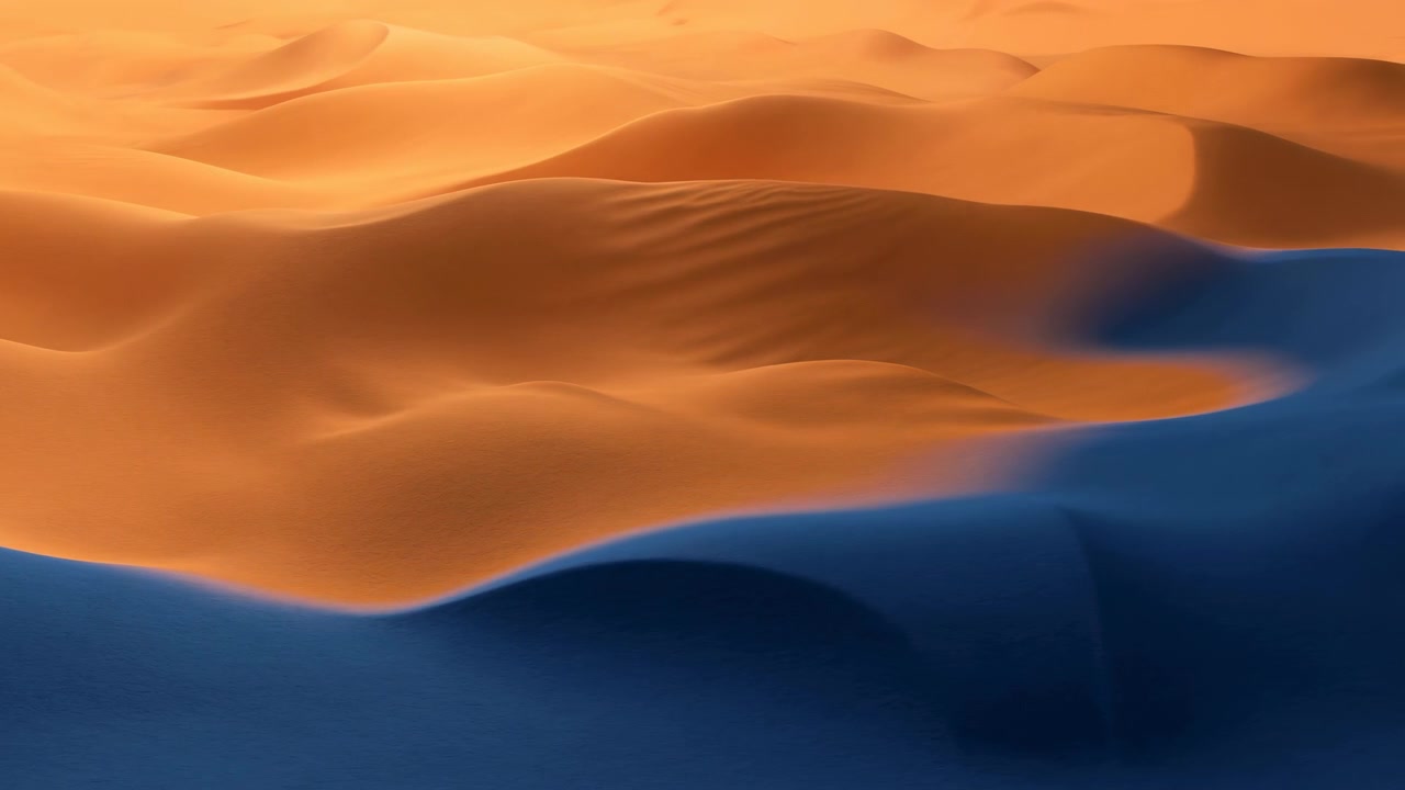 Vista panoramica del deserto con dune dolcemente ondulate, creste dorate e luminose, avvallamenti profondamente ombreggiati di blu e una texture di sabbia fluida che crea un contrasto calmo, profondità e una forma naturale spaziosa