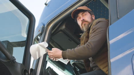 bottom view of worker wearing vest and cap organizing a truck fleet in a logistics park while reading documents in a truck