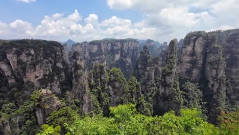 pan left view of towering cliffs covered in dense vegetation under a partially cloudy sky