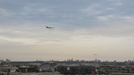 Urban-landscape,-tracking-shot-capturing-two-commercial-airplanes-flying-low-in-the-sky,-prepare-to-land-at-Toronto-pearson-international-airport,-Mississauga,-Ontario,-Canada