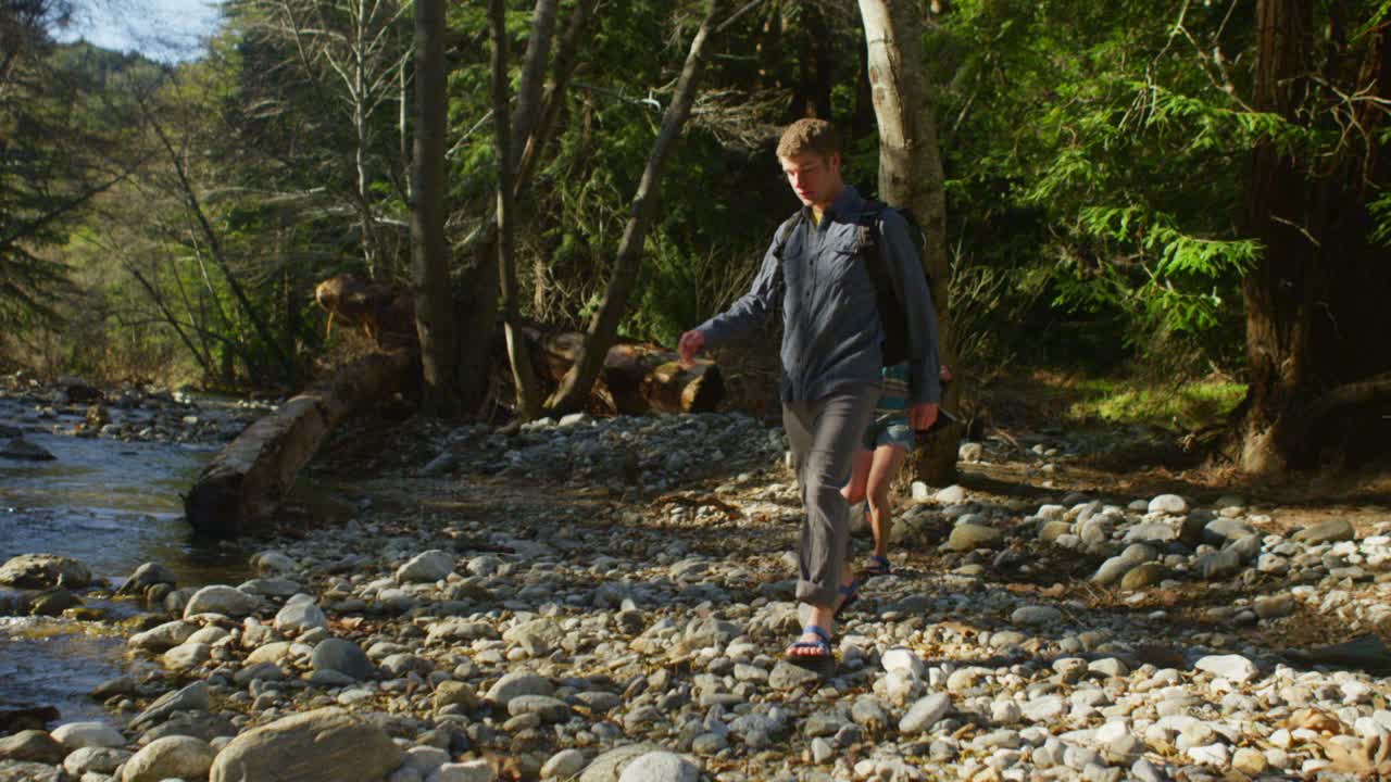 한 커플이 숲속의 바위 개울을 향해 걸어간다