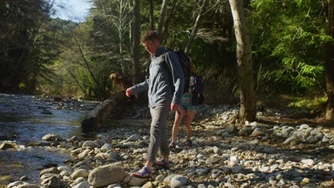 A-couple-walks-towards-a-rocky-stream-in-a-forest