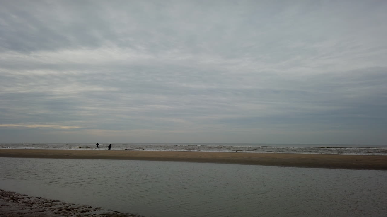 Silhouette of a family walking along a beach on a cloudy day. Two people watching waves on a coastal beach.